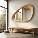 May include: A wooden bench with a light brown leather seat and a unique, organic design. The bench is in front of a large, oval-shaped mirror with a wooden frame.
