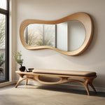 May include: A modern, organic-shaped wooden mirror with a light-colored frame hangs above a matching bench. The bench has a cushioned seat and a unique, flowing design. A small plant in a dark pot sits on the bench, adding a touch of nature to the space.