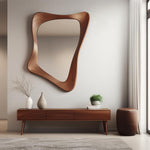 May include: A wooden console table with three drawers, a brown leather ottoman, and a large, abstract, wooden framed mirror on a white wall.  The console table has a light wood finish and the ottoman is round.