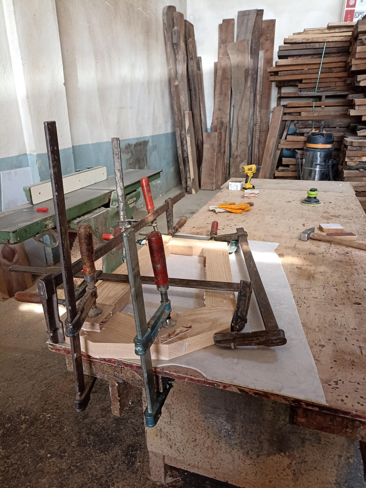 May include: A woodworking project in progress, with several pieces of wood being clamped together using metal clamps. The wood is light brown and the clamps are silver and black. The project is being worked on in a workshop setting.