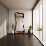 May include: A modern, wooden, free-form mirror with a wavy design. The mirror is standing in a room with a light brown floor, a white wall, and a large window with a view of a green lawn.