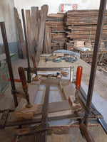 May include: A wooden frame is being assembled using clamps. The frame is made of light and dark wood and is being held together by metal clamps with red handles. The frame is sitting on a workbench in a workshop.