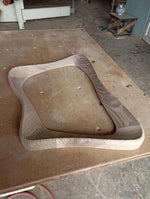 May include: A wooden frame for a chair or table, with a wavy, organic shape. The frame is made of light and dark wood, and is unfinished.