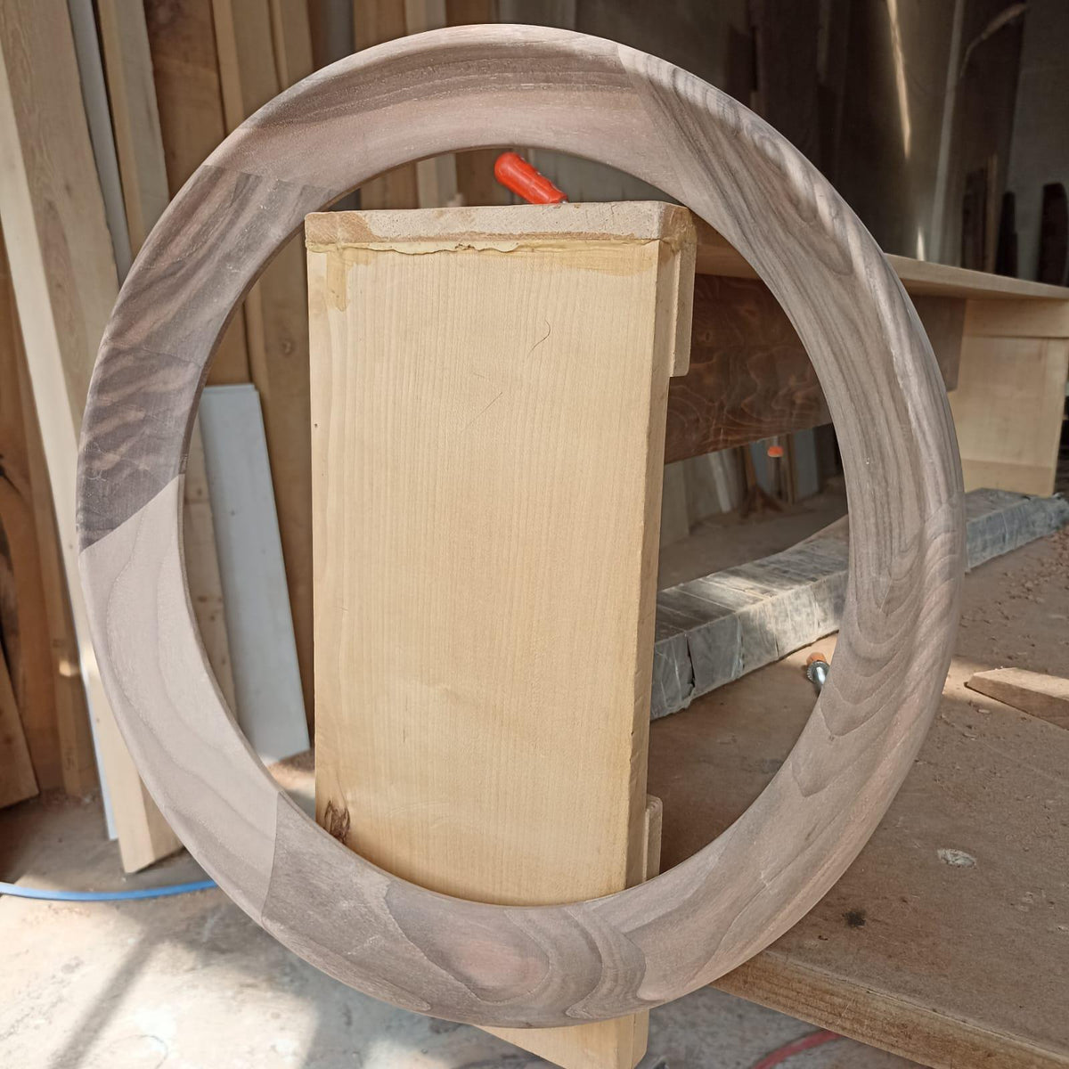 May include: A round wooden frame made of walnut wood with a natural wood finish. The frame is being used to create a circular opening in a piece of wood.