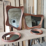 May include: Three wooden framed mirrors with wavy edges. The largest mirror is a light brown color and the two smaller mirrors are a darker brown. The mirrors are all sitting on a light brown wooden surface.