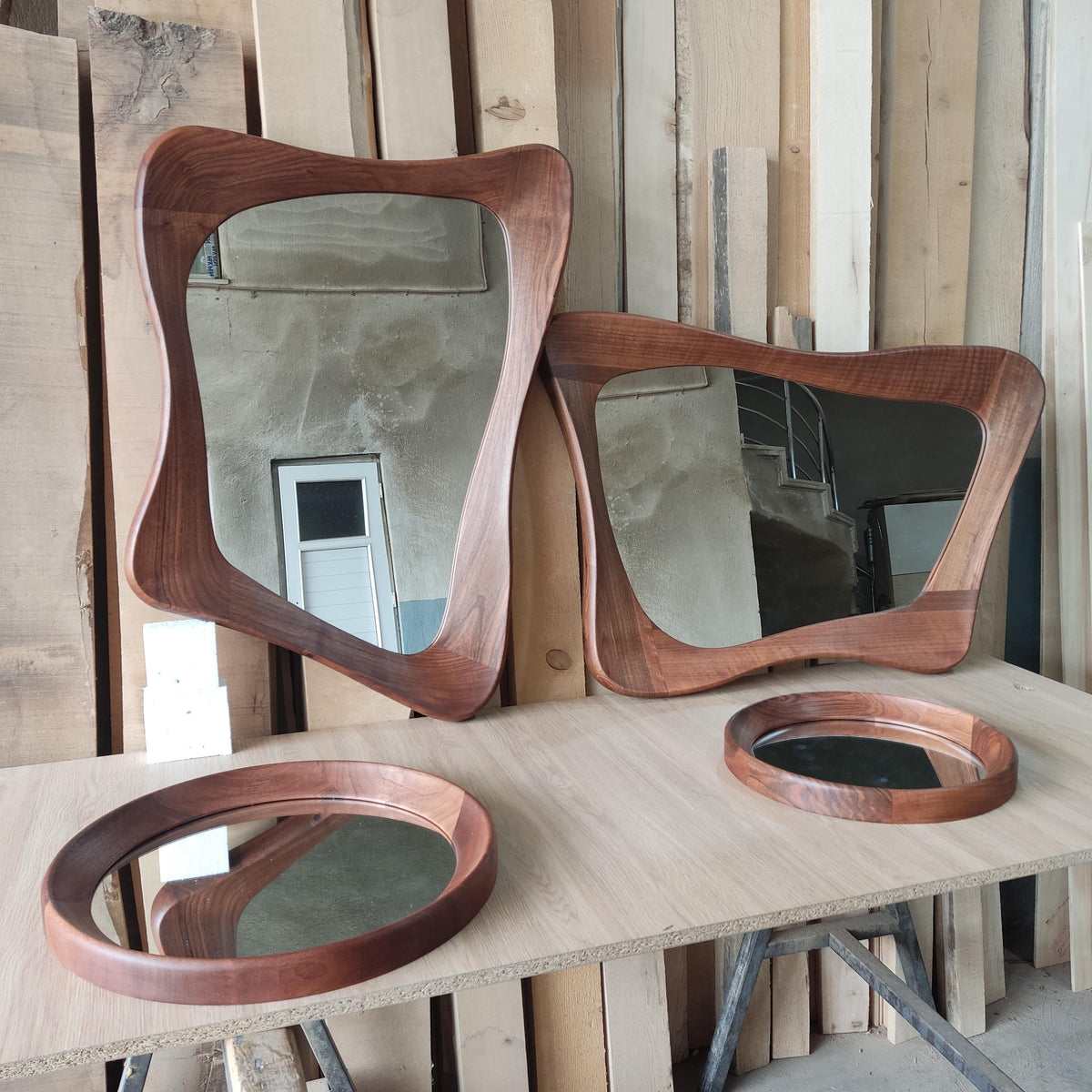 May include: Three wooden framed mirrors with wavy edges. The largest mirror is a light brown color and the two smaller mirrors are a darker brown. The mirrors are all sitting on a light brown wooden surface.