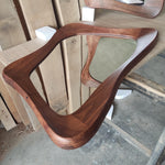 May include: A wooden mirror with a unique, organic shape. The mirror is made of dark wood and has a smooth, polished finish.