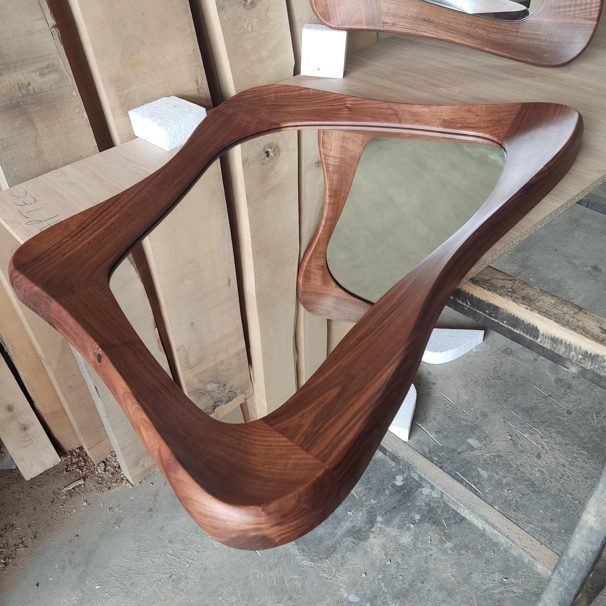 May include: A wooden mirror with a unique, organic shape. The mirror is made of dark wood and has a smooth, polished finish.