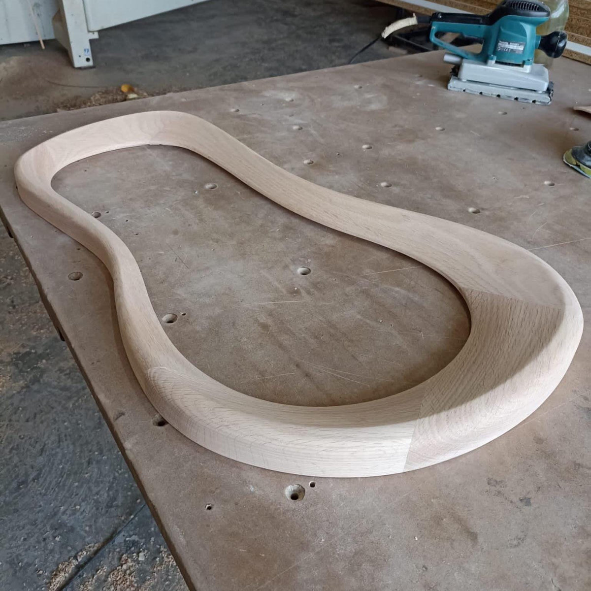 May include: A light wood curved frame, possibly for a chair or table, is sitting on a wooden workbench.