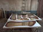 May include: A collection of wooden framed mirrors in various shapes and sizes, including oval, rectangular, and freeform designs. The mirrors have a brown wood trim and are set against a white background. The pieces are displayed on a work table.
