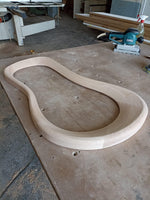 May include: A light wood curved piece of wood, likely for furniture making, on a wooden workbench.