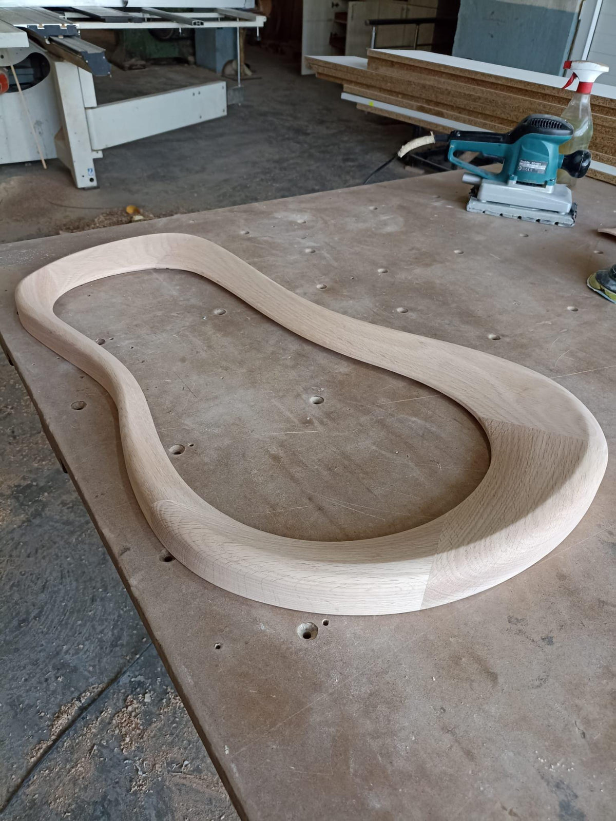 May include: A light wood curved piece of wood, likely for furniture making, on a wooden workbench.