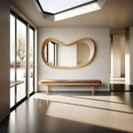 May include: A modern interior featuring a large, organically shaped wooden mirror mounted on a white wall. Below the mirror is a wooden bench with a brown cushion. Large windows and a skylight provide natural light, creating a bright and airy space.