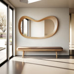 May include: A modern interior scene featuring a large, organically shaped wooden mirror mounted on a white wall. Below the mirror is a wooden bench with a brown cushion. The room has large windows and a minimalist design.