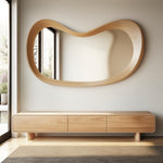May include: A large, organically shaped wooden mirror hangs above a matching wooden cabinet with three drawers. The mirror's frame has a smooth, flowing design. The cabinet sits on short, rectangular legs. The room has a modern, minimalist aesthetic.