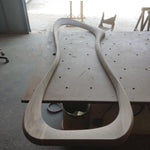 May include: A large, unfinished, wooden frame with a curved, organic shape. The frame is resting on a gray surface.