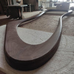 May include: A dark brown wooden frame with a unique, curved, and asymmetrical design. The frame is made of solid wood and has a smooth, polished finish.