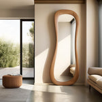 May include: A large, free-form wooden mirror with a wavy, organic shape. The mirror is standing against a light beige wall in a modern interior.