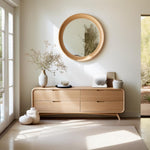 May include: A light wood dresser with four drawers and rounded edges. The dresser has a curved front and sits on angled legs. A round wood framed mirror hangs above the dresser. Two white ceramic vases and a small bowl sit on top of the dresser.