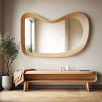 May include: A wooden bench with a curved design and a shelf underneath. The bench is made of light wood and has a natural finish. A throw blanket is draped over the bench. A large, wavy, wooden framed mirror hangs on the wall behind the bench.