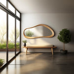 May include: A wooden bench with a light brown cushion sits in front of a large, organic-shaped mirror with a wooden frame. A small potted plant sits on the bench and a larger potted plant is in the corner of the room.
