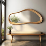 May include: A wooden bench with a light beige cushion sits in front of a large, organic-shaped wooden mirror. The mirror is mounted on a white wall.