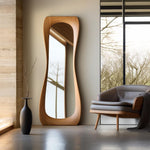 May include: A full-length wooden mirror with a unique, curved design. The mirror is standing in a room with a large window and a gray armchair.