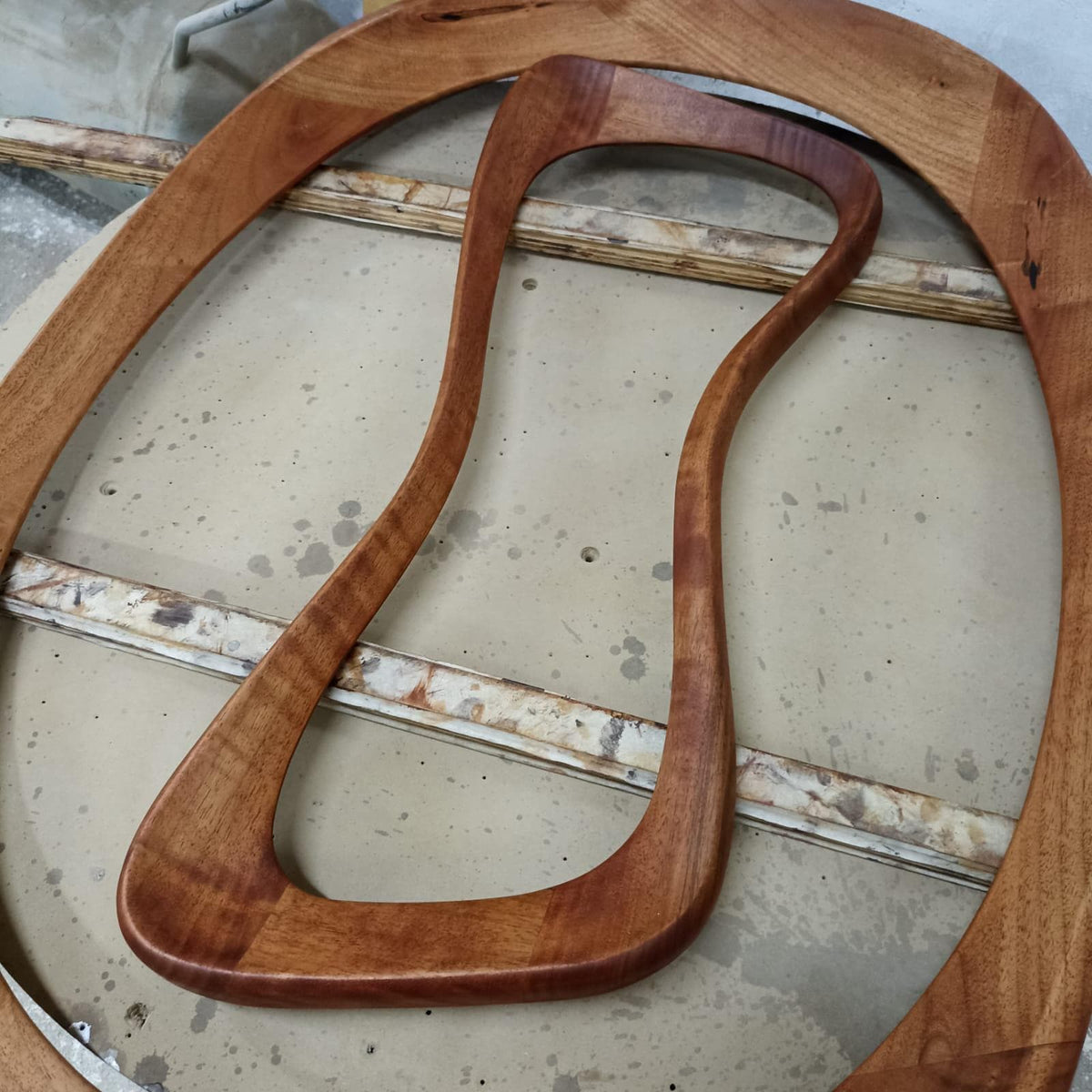 May include: Two wooden frames and a curved wooden handle. The frames are oval-shaped, and the handle has a unique, ergonomic design. The wood has a warm, reddish-brown hue, with visible grain patterns. The items appear to be handmade.