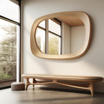May include: A modern interior scene featuring a large, oval-shaped wooden mirror mounted on a light-colored wall. Below the mirror is a matching wooden bench with a curved design. A small, round ottoman sits to the left of the bench. The room has large windows.