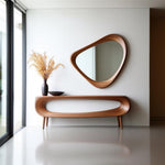 May include: A modern wooden console table with a unique curved design, featuring a matching organic-shaped mirror. The table has a dark vase with dried flowers and a small black bowl. The mirror is approximately 30 inches wide.