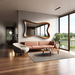May include: A modern living room featuring a large, uniquely shaped wooden mirror above a blush-colored sofa. A gray armchair, a round coffee table, and a potted plant complete the space. Large windows offer a view of the outdoors.