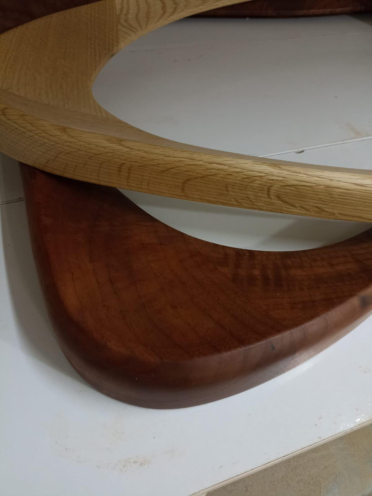 May include: Close-up of two wooden, curved objects. One is a light-colored wood, the other is a darker, reddish-brown wood. The objects appear to be part of a larger piece of furniture or decor, possibly a table or a decorative element.