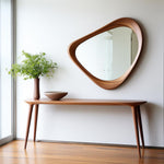 May include: A mid-century modern style wooden console table with a matching mirror. The mirror has an organic, asymmetrical shape. A vase with greenery and a bowl sit on the table. The room has a minimalist design.