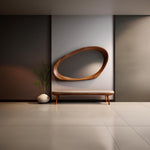 May include: A modern interior scene featuring a wooden oval mirror mounted on a light gray wall. Below the mirror is a bench with a cream-colored seat and wooden legs. A white vase with greenery sits to the left.