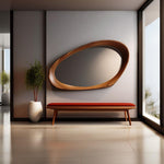 May include: A modern interior scene featuring a large, oval-shaped wooden mirror with a natural wood grain finish. Below the mirror is a bench with a red cushion and wooden legs. A potted plant sits to the left, and a window is on the right.