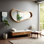 May include: A large, organically shaped wooden mirror with a light-colored frame hangs on a gray wall. Below, a wooden bench with a cream-colored cushion and two drawers sits. A small stool and a potted plant are also in the room.