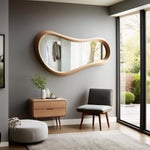 May include: A modern living room featuring a large, uniquely shaped wooden mirror. The mirror hangs on a gray wall above a wooden nightstand with two drawers. A gray chair and a round ottoman are also in the room.