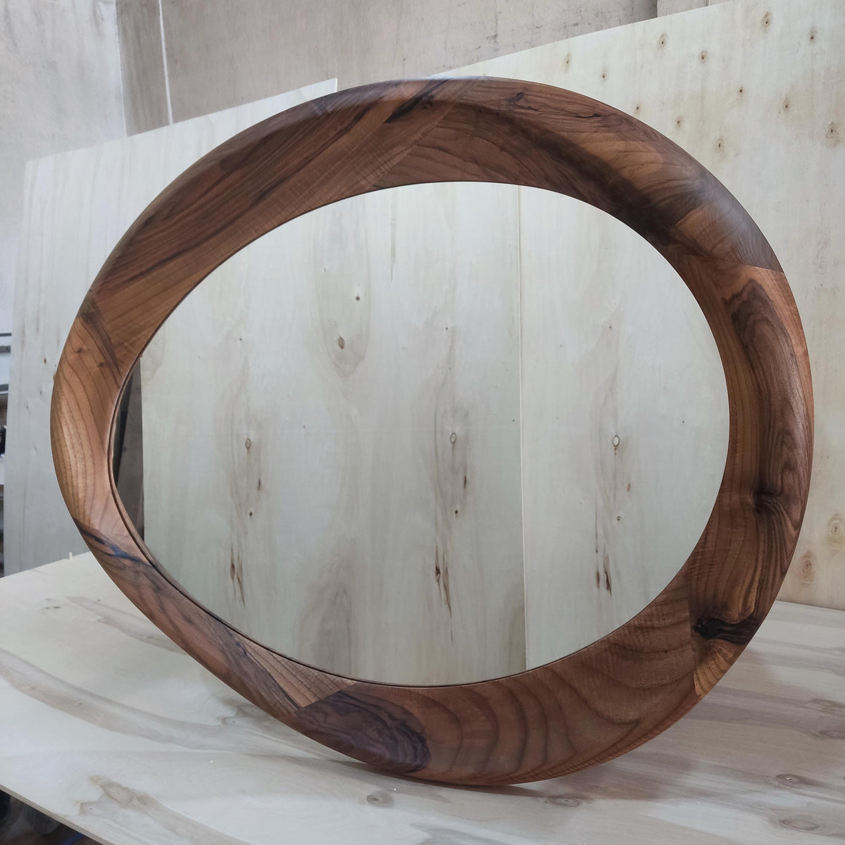 May include: Oval-shaped wooden mirror with a dark brown, natural wood grain finish. The frame is thick and curved, creating a modern, organic design. The mirror is approximately 30 inches in diameter, perfect for a bedroom or living room.