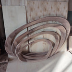 May include: A set of four wooden oval-shaped frames, each nested within the other. The wood has a natural grain pattern with varying shades of brown and tan. The frames are arranged against a backdrop of wooden panels.