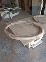 May include: Two unfinished wooden circular frames with a natural wood grain pattern sit on a workbench. The frames are thick and appear to be part of a larger woodworking project. The workshop setting includes tools and equipment.