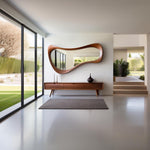 May include: A mid-century modern interior featuring a large, organically shaped wooden mirror above a wooden console table. The room has a minimalist design with a gray rug, two white vases, and a black vase. Large windows offer a view of the outdoors.