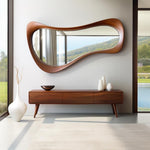 May include: A mid-century modern-style interior featuring a large, organically shaped wooden mirror. Below, a matching wooden console with three drawers and tapered legs is visible. White vases and a dark bowl add contrast.