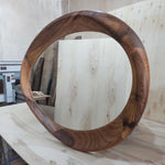 May include: A large, round mirror with a unique, organic wooden frame. The frame is crafted from dark brown wood, showcasing the natural grain and texture. The mirror reflects the surrounding environment, adding depth and dimension to any space. The design is modern and artistic.