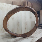 May include: A large, oval-shaped wooden mirror with a unique, flowing design. The frame is crafted from dark, rich-toned wood, creating a striking contrast against the light-colored background. The mirror's dimensions are approximately 30 inches in diameter.