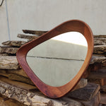 May include: A mid-century modern style mirror with a unique, organic shape. The frame is crafted from rich, dark wood, and the mirror's surface reflects the light. The design is a blend of form and function, suitable for any room.