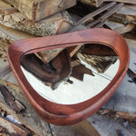 May include: A mid-century modern style mirror with a unique, organic shape. The frame is made of rich, dark wood, and the mirror has a smooth, reflective surface. The mirror is approximately 20 inches wide and 15 inches tall.