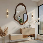 May include: A modern entryway featuring a large, organically shaped wooden mirror. Below, a light wood bench with a cushioned seat and a matching cabinet with closed doors and open shelving. A gold floor lamp and wall sconces provide lighting.
