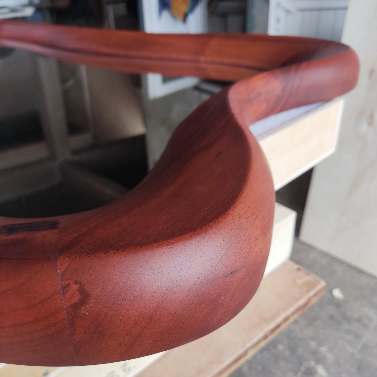 May include: A curved, wooden furniture component with a rich, reddish-brown finish. The piece has a smooth, polished surface and a flowing, organic shape. The wood grain is visible, adding to the natural aesthetic. The component appears to be part of a larger structure.