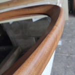 May include: Close-up of a wooden framed mirror. The frame is made of a light brown wood with a smooth, curved design. The mirror's surface reflects the surrounding environment.