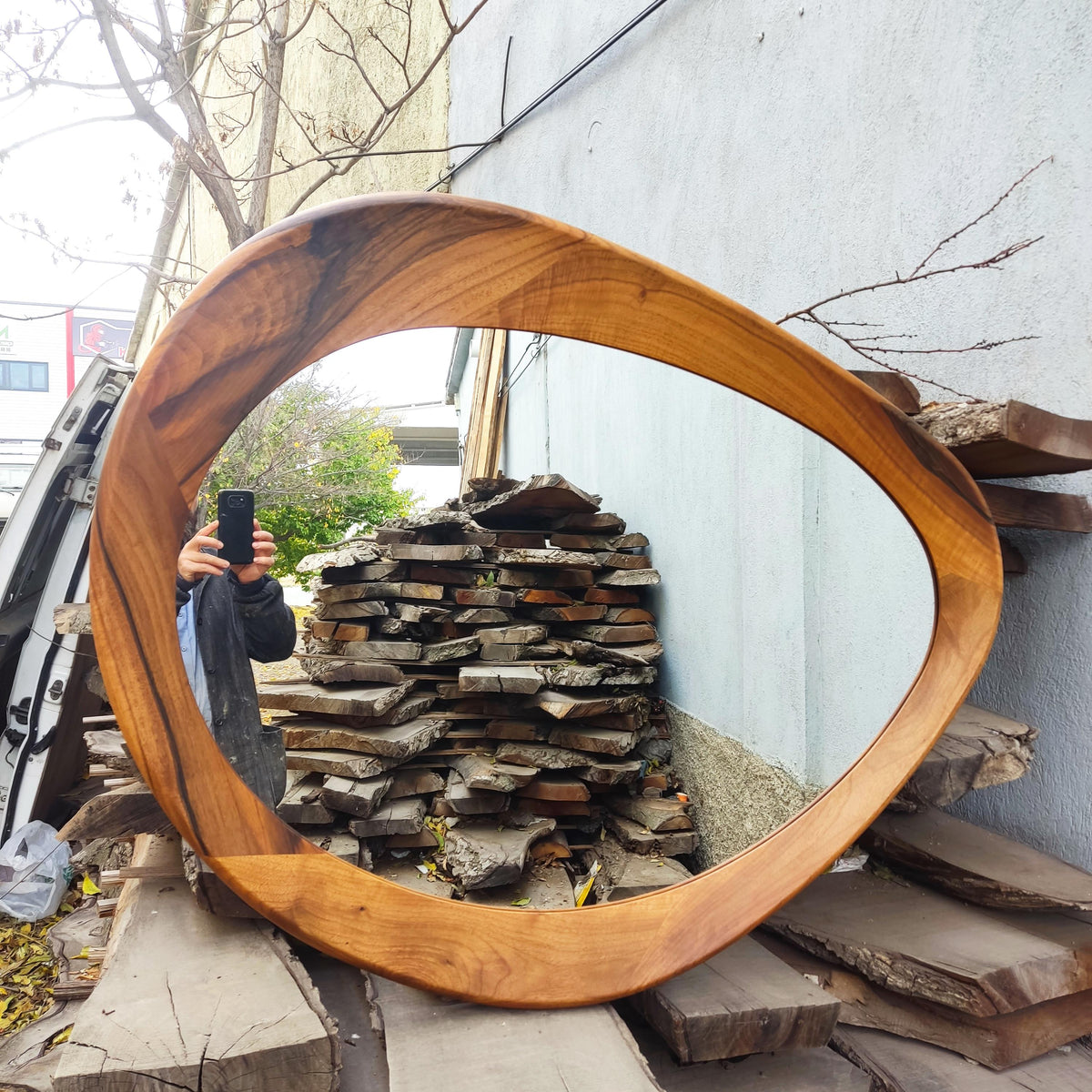 May include: A large, oval-shaped wooden mirror with a natural wood grain finish. The frame has a unique, flowing design. The mirror reflects the surrounding environment. The mirror is a decorative home decor item.